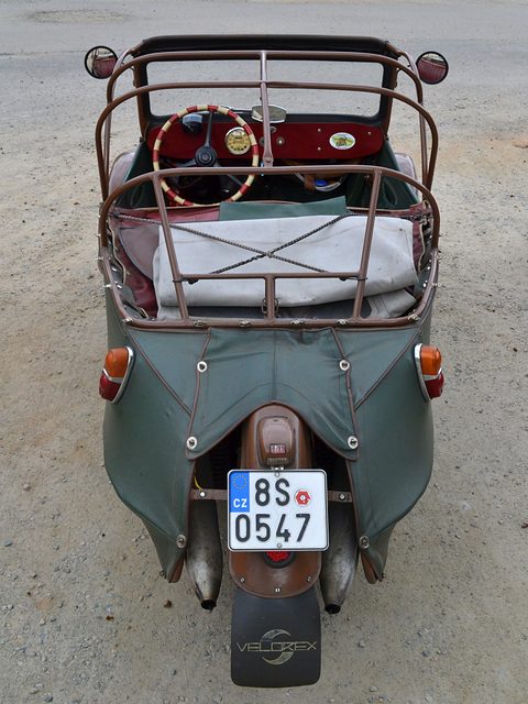 Overhead rear view of a green three-wheeler: single rear wheel, twin silencers, mudflap, red dashboard and cream steering wheel. Opens a larger view