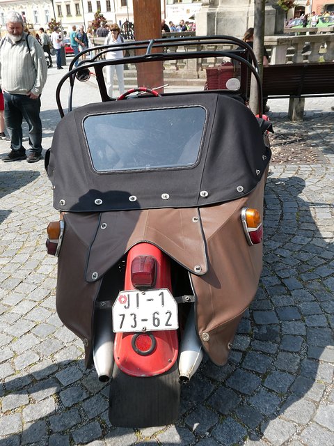 Rear of a brown three-wheeler with black fabric rear hood, red mudguard, twin silencers and Czechoslovak plate. Opens a larger view