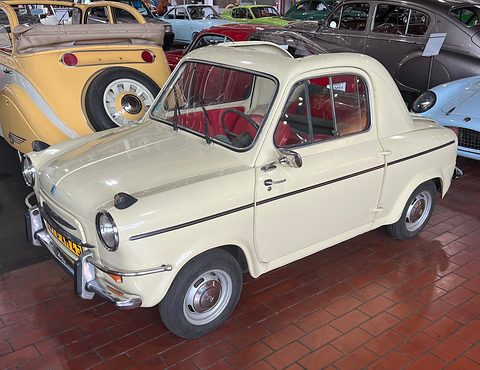 Cream small car with a black waistline stripe on a red tiled floor, a yellow open car beside it. Opens a larger view