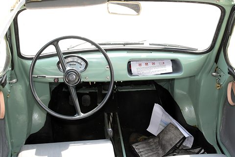 Painted pale green dashboard with a large thin two-spoke steering wheel, a round speedometer and a parcel shelf. Opens a larger view