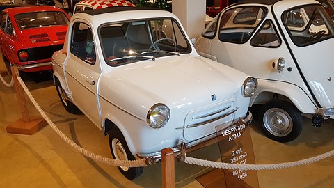 White small car behind a rope barrier with a glass placard reading VESPA 400 ACMA, 2 cyl., 393 cm3. Opens a larger view
