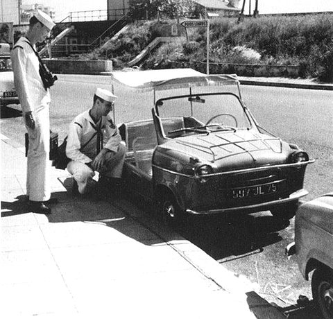 Black and white photograph of two sailors in white uniforms beside an open doorless car with a fringed canopy and Paris plate.