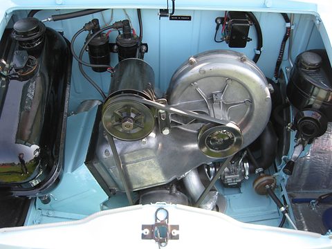 Clean engine bay with a silver finned fan housing, drive belt, black ignition coils and a fuel tank at the left. Opens a larger view