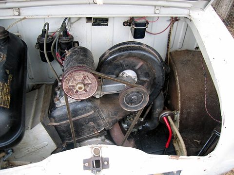 Grimy engine compartment with a rusty pulley and belt, a black fan housing and a fuel tank at the left. Opens a larger view