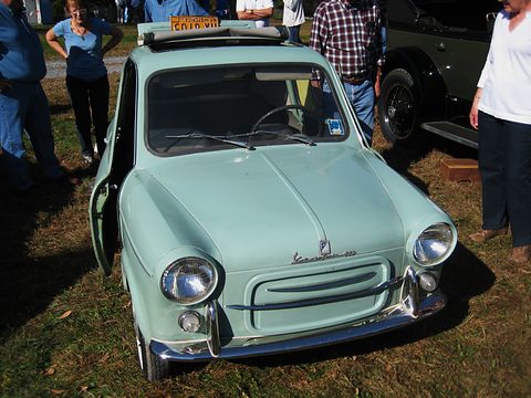 Mint green small rounded car with large round headlamps and a chrome bumper on grass, spectators standing round it. Opens a larger view