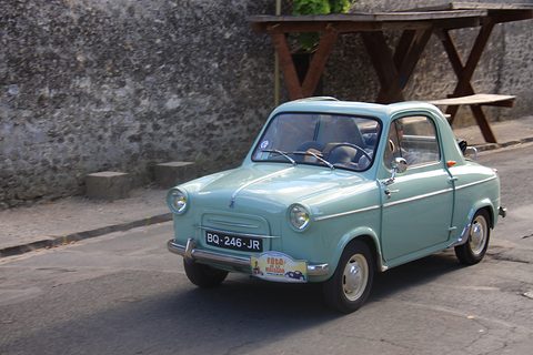 Mint green small car with plate BQ-246-JR on a road beside a stone wall and wooden picnic table. Opens a larger view