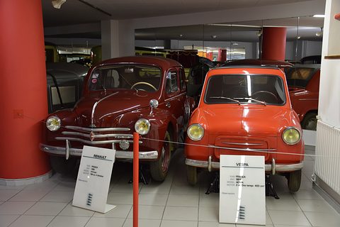 Orange small car and a dark red Renault 4CV side by side behind a rope, each with a placard in front. Opens a larger view