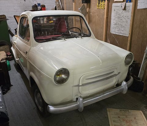Cream small car parked in a cluttered workshop with old road maps and tools on the walls. Opens a larger view