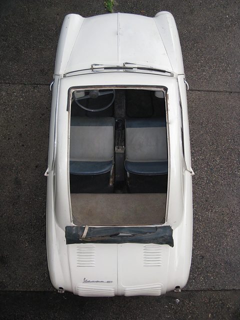 Top-down view of a white small car with its fabric roof folded at the back, showing two seats and the luggage shelf. Opens a larger view