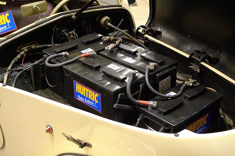 Black batteries joined by heavy cables, packed into the cream nose of the car under its raised bonnet.