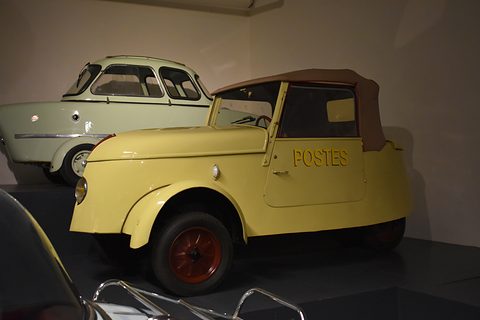 Yellow two-seater lettered POSTES with red wheels and a brown hood, a pale green bubble car parked behind. Opens a larger view