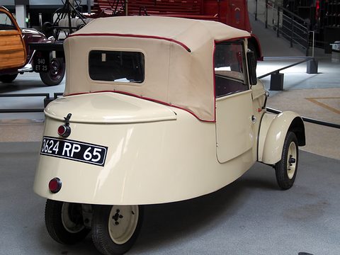 Rear three-quarter of a cream car with a small window in its fabric hood, plate 3624 RP 65 and closely set rear wheels.