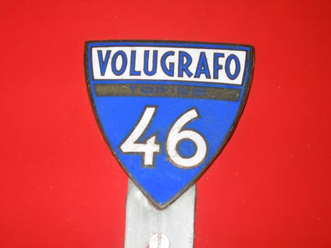 Blue and white enamel shield reading VOLUGRAFO above a large 46, on red paint. Opens a larger view