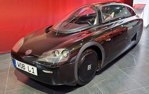 Long, low black two-seat streamliner with a glass canopy and covered rear wheels on a grey tiled floor. Opens a larger view