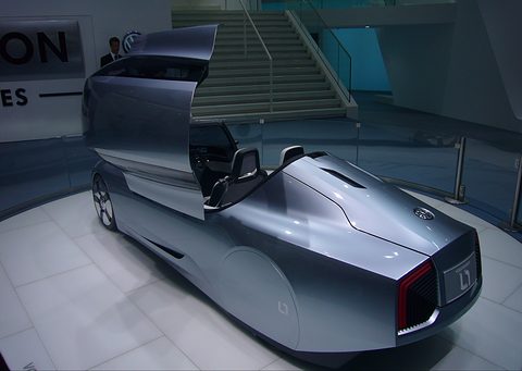 Silver tapered tail of a tandem two-seater with a slim lamp bar and its canopy lifted, on a white floor. Opens a larger view