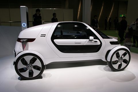 Side view of a white single-seat concept with exposed wheels and a long side window on a white floor. Opens a larger view