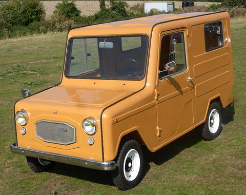 Small ochre boxy van with a mesh grille panel, round headlamps and white wheels, standing on grass. Opens a larger view