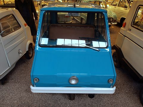 Front view of a narrow turquoise microcar with a flat nose, a white bumper and a large upright windscreen. Opens a larger view