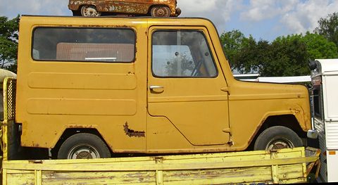 Side view of a rusty ochre van with sliding side windows on a yellow flatbed trailer. Opens a larger view