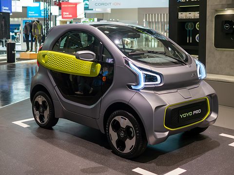 Grey two-seat microcar with lime-green door bar and a YOYO PRO badge on its front on a stand. Opens a larger view