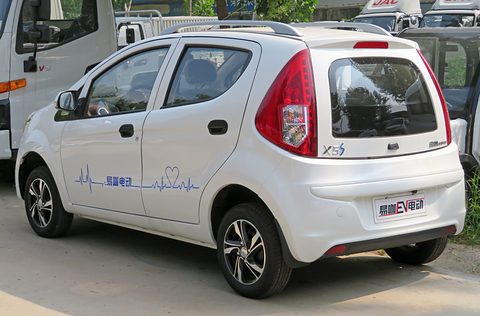 Rear of a white small four-door hatchback with a blue heartbeat graphic on its doors on a dusty lot. Opens a larger view