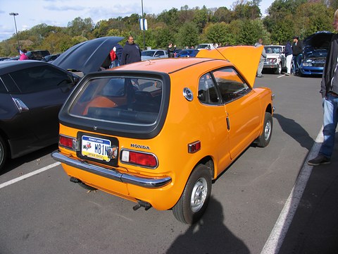 Rear three-quarter of an orange hatchback with a Pennsylvania plate, parked cars around. Opens a larger view