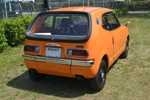 Rear view of an orange hatchback with a black-framed rear window, parked on grass. Opens a larger view