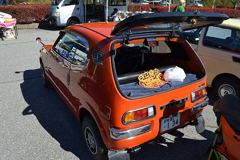 Orange hatchback with the rear glass raised over a small luggage area holding bags. Opens a larger view