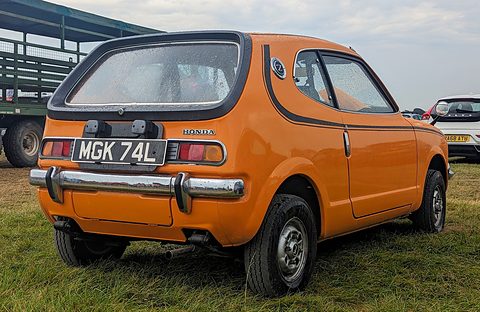 Rear view of an orange hatchback with a black-framed rear window and a UK number plate, on grass. Opens a larger view