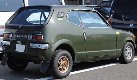 Rear three-quarter of a dark olive hatchback with a black-framed rear window and HONDA lettering. Opens a larger view