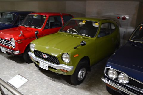 Lime-green small coupé between a red car and a dark car in a museum row. Opens a larger view