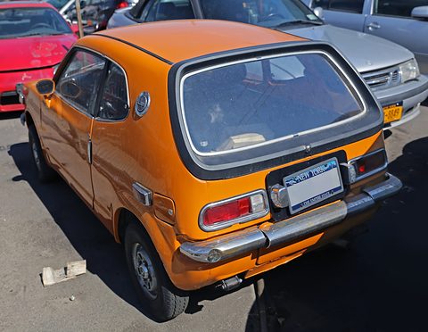 Rear view of an orange hatchback with a US plate on the tail panel, in a car park. Opens a larger view
