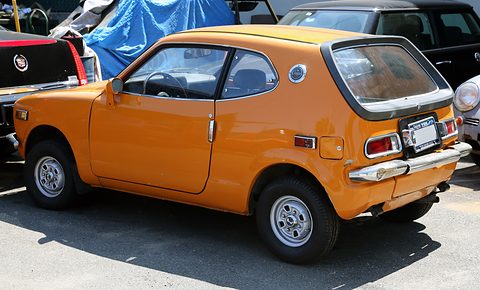 Rear three-quarter of an orange hatchback parked among other cars in a car park. Opens a larger view