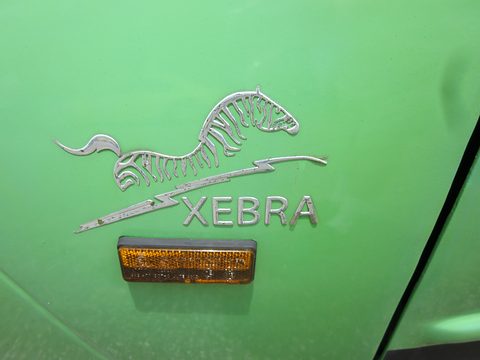 Close view of a chrome badge of a leaping zebra and lightning bolt above the word XEBRA and an amber reflector. Opens a larger view