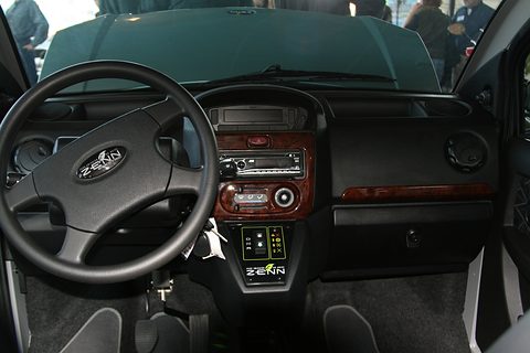 Black dashboard with a ZENN steering wheel, wood-effect centre panel and car radio, seen through the open door. Opens a larger view