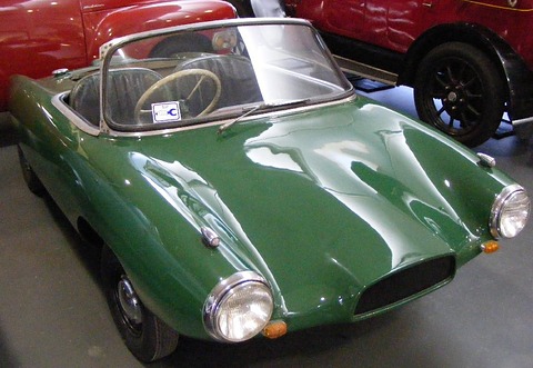 Green doorless roadster with a low curved windscreen and faired headlamps, among other museum cars.